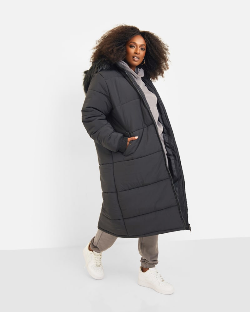 Side of a model wearing a size 4X Aspen Hooded Puffer Coat in Black by Rebdolls. | dia_product_style_image_id:324224